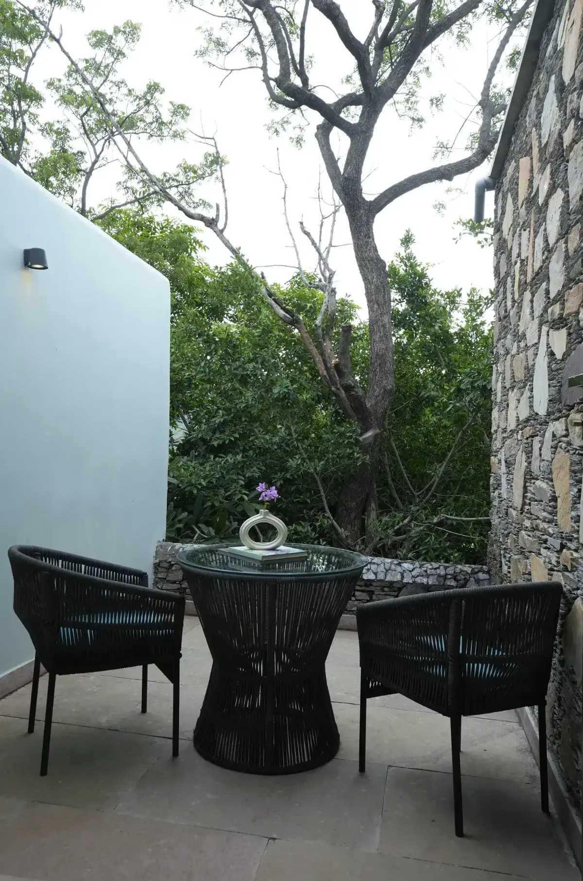 Shaded courtyard seating beside a stone wall and old tree