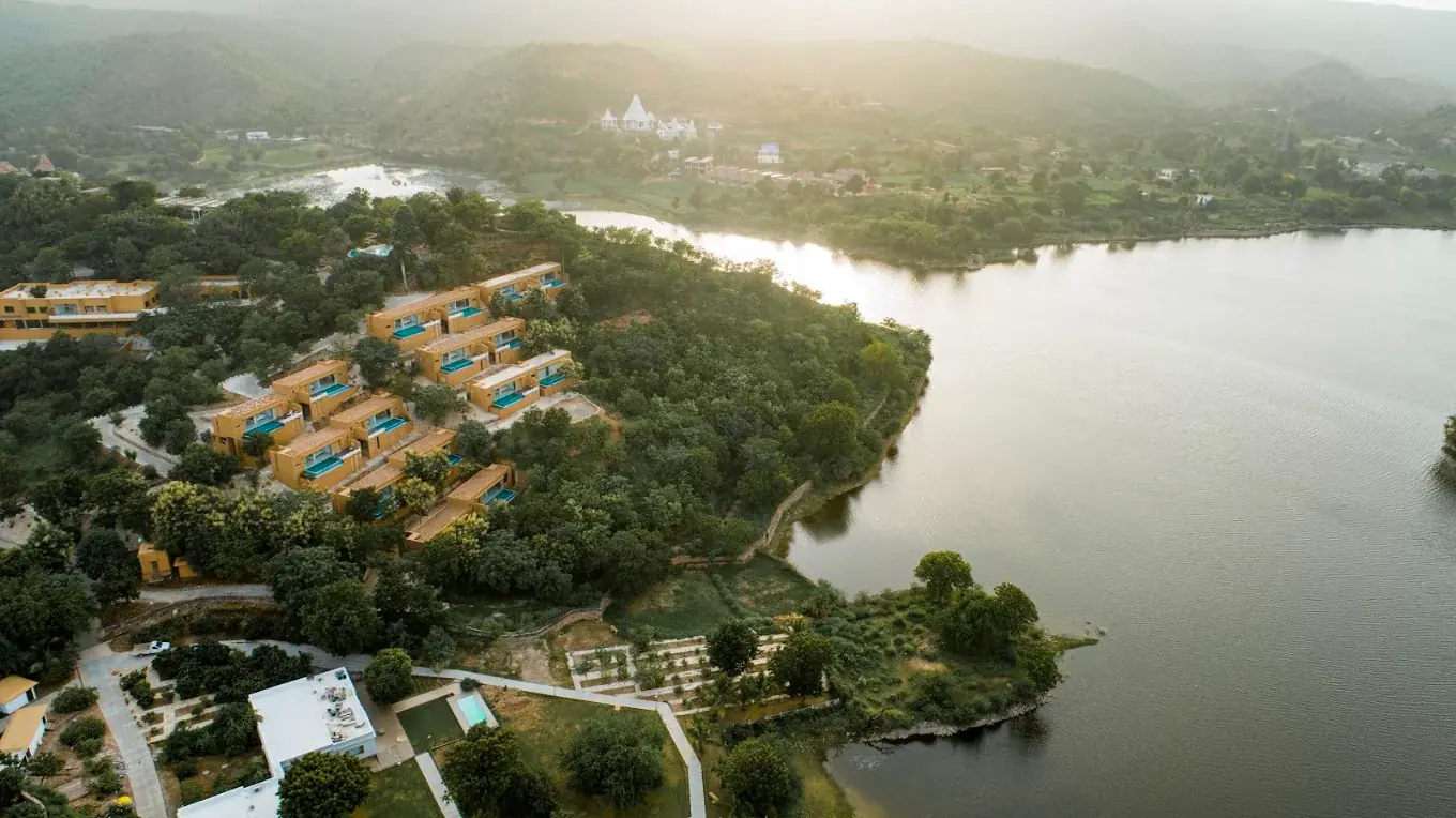 Aerial view of YAAN Udaipur resort nestled on the edge of Bagela Lake with the Aravalli hills in the distance